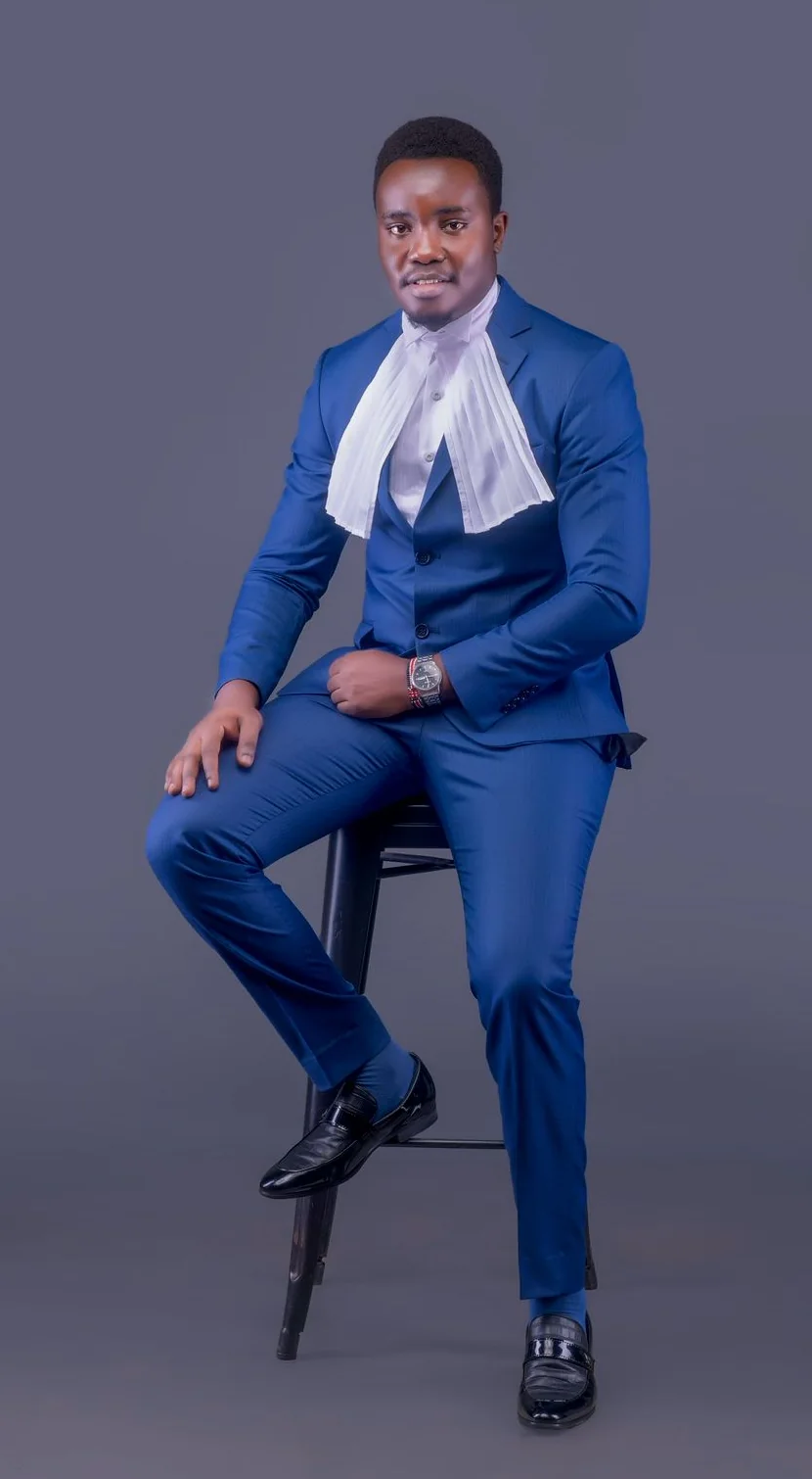 The advocate seated on a stool in a blue three-piece suit and white bands, photographed in a studio